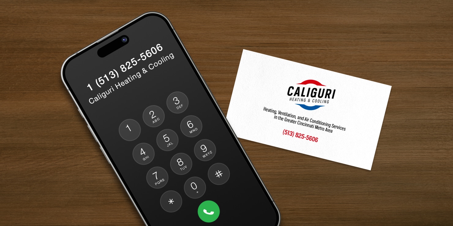 Mobile phone with Caliguri Heating & Cooling phone number on the screen and a business card with the phone number 513-825-5606